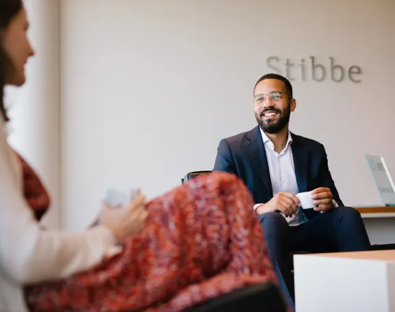 Male Stibbe lawyer in business suit smiling while chatting with a female colleague at the reception of Stibbe in Brussels