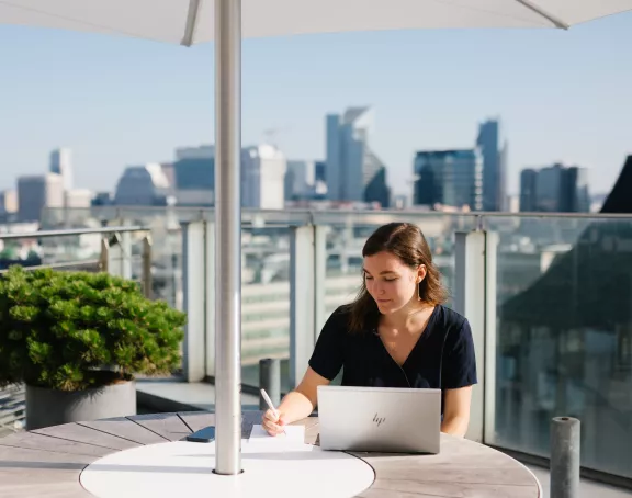 Female Stibbe lawyer taking notes in front of her laptop at the rooftop bar of Stibbe in Brussels