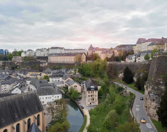 Panoramic view of Grund in Luxembourg City, showcasing a picturesque scene with historic buildings, lush greenery, and the Alzette River flowing through the charming district