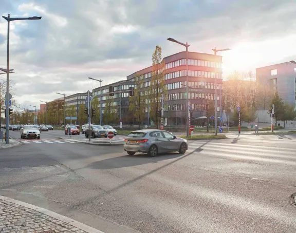 Cars drive along a wide street lined with modern buildings in Luxembourg City, where bike lanes, traffic lights, and trees border the sidewalk