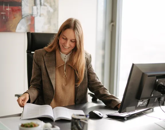 A female Stibbe lawyer sitting at her desk, smiling as she flips through a book.