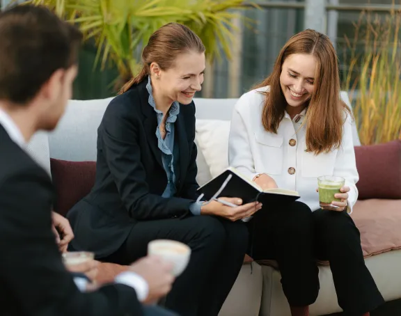 Two male Stibbe lawyers and two female Stibbe lawyers sitting on an outdoor sofa. The men have their backs to the camera, while the women are smiling and looking at a notebook held by one of them.