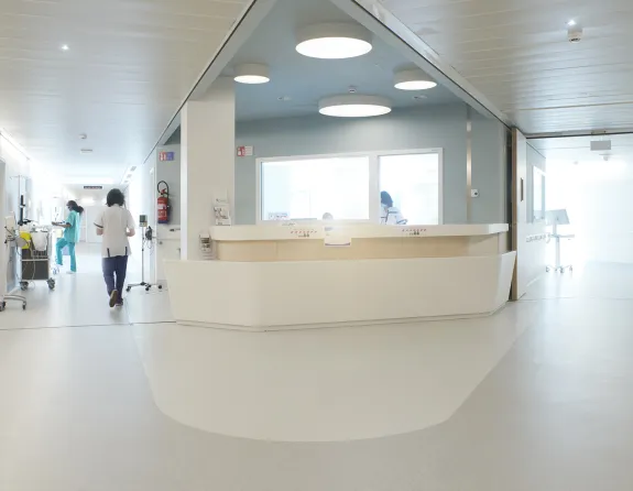 Hospital corridor with staff members walking around, an info desk, medical equipment and patient rooms