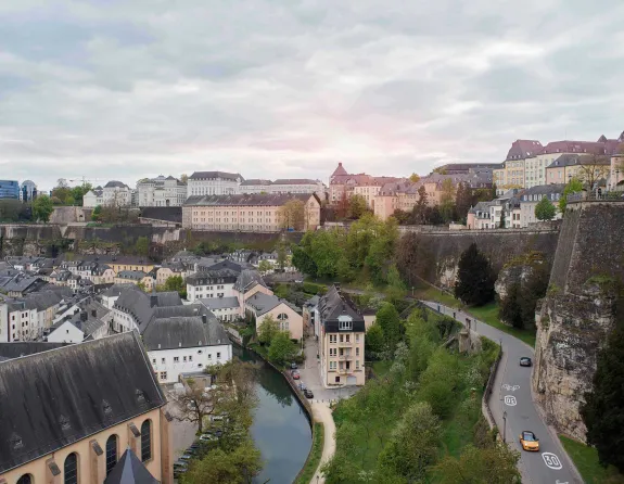 Panoramic view of Grund in Luxembourg City, showcasing a picturesque scene with historic buildings, lush greenery, and the Alzette River flowing through the charming district