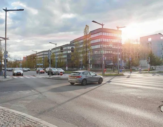 Cars drive along a wide street lined with modern buildings in Luxembourg City, where bike lanes, traffic lights, and trees border the sidewalk