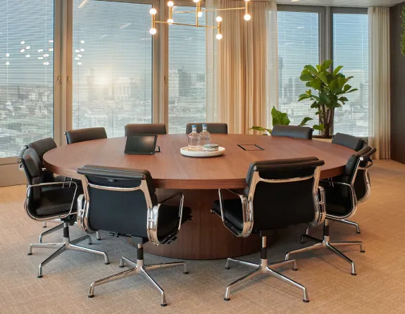 Modern conference room at Stibbe with a round wooden table, black leather chairs, large windows and a TV screen.