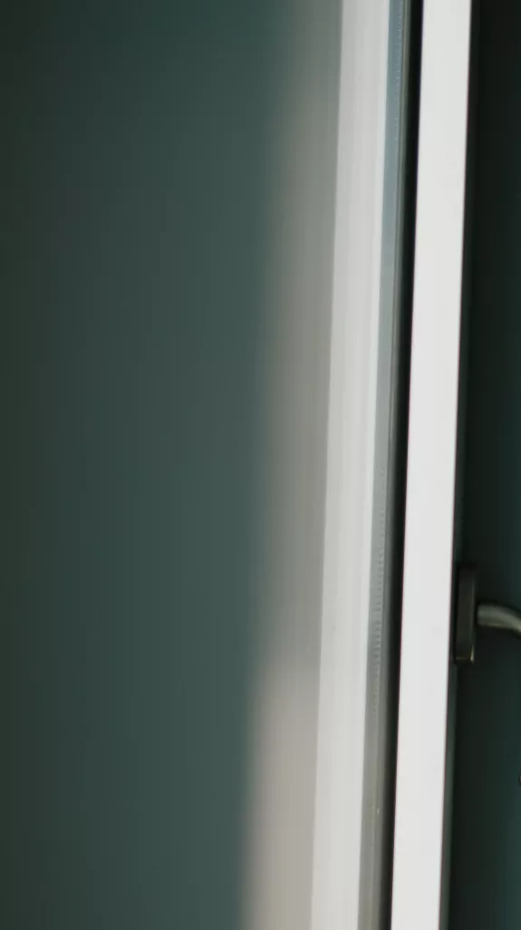 Female Stibbe employee looking through the window of a meeting room at Stibbe in Brussels while holding her smartphone with both hands