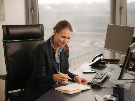 A female lawyer is working at her desk, writing notes in a notepad.