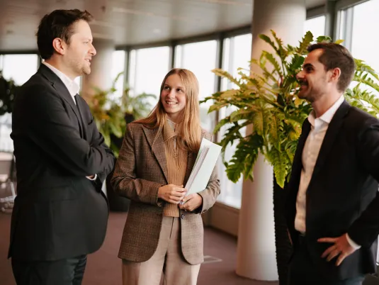 Three co-workers, two men and one woman, are engaging in a friendly conversation. They are smiling and appear to be enjoying the discussion.