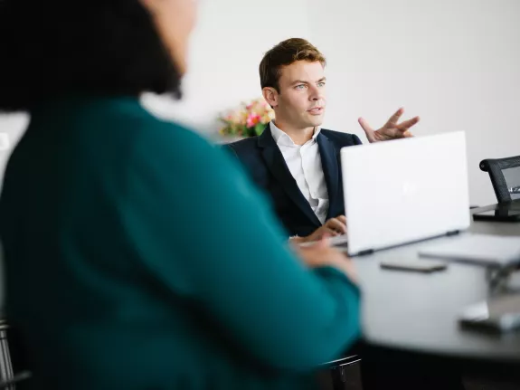 Male Stibbe lawyer sitting at the table talking to colleagues from behind his laptop in a meeting room at Stibbe in Brussels